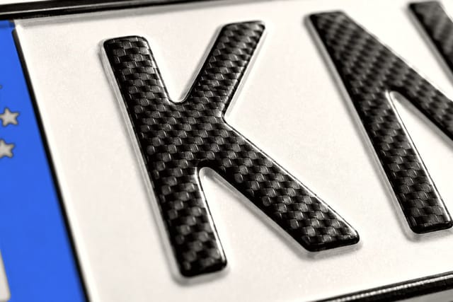 Nahaufnahme geprägter Buchstaben in Kohlefaser-Optik auf einem Kennzeichen