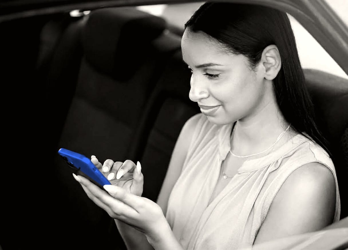 Frau sitzt im Auto und erledigt die Zulassung auf dem Smartphone